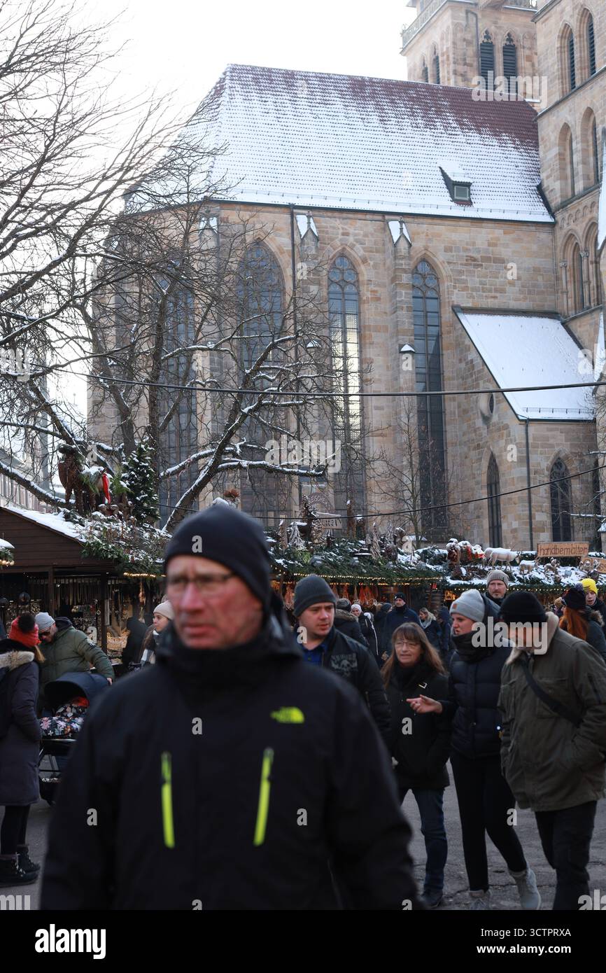 Stoccarda, Germania - 18 dicembre 2022, i visitatori passeggiano attraverso un tradizionale mercatino di Natale adagiato contro una cattedrale storica, con tetti innevati e. Foto Stock