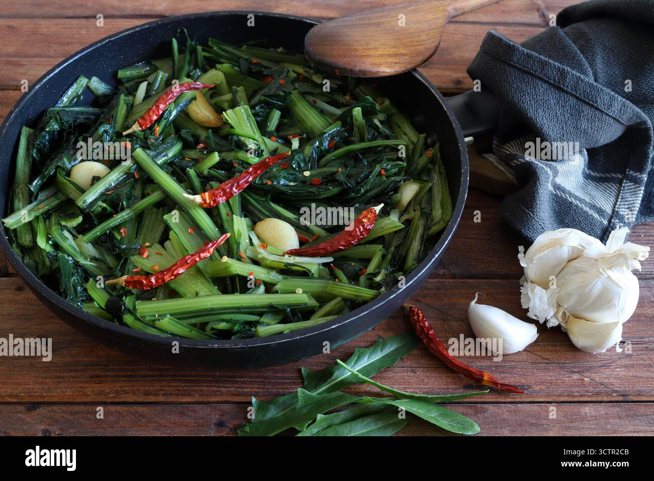Verdure di cicoria saltate all'italiana con aglio e peperoni caldi in padella su fondo rustico. Contorno italiano.cibo sano e vegetariano. Vista dall'alto Foto Stock