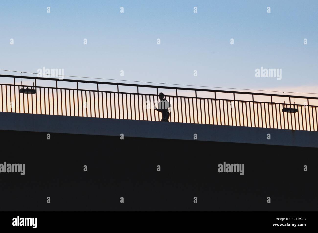 Cielo tramonto color pastello con silhouette a contrasto di una persona che corre sul ponte Rheinkniebrücke Foto Stock