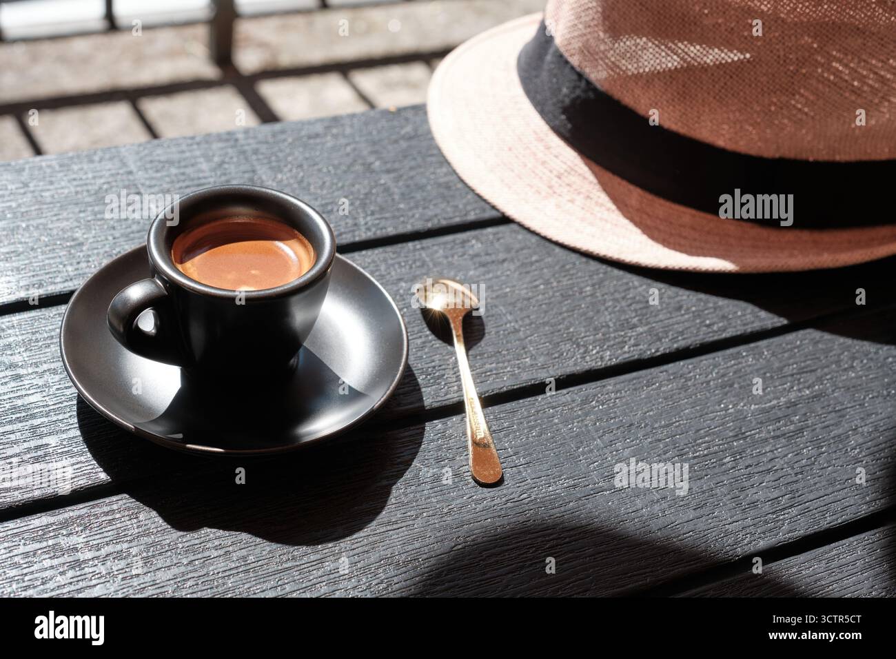 Tazza di caffè espresso con cucchiaio e cappello estivo su un tavolo di legno alla luce del sole, simbolo dello stile di vita italiano e del relax. Foto Stock