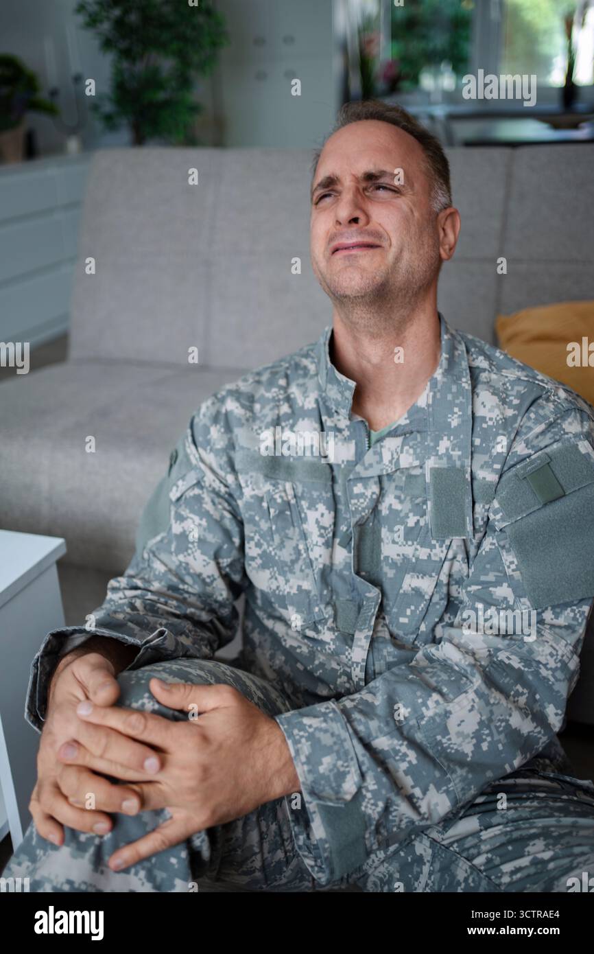 Soldato depresso che piange da solo a casa soffrendo di disturbo da stress post-traumatico Foto Stock
