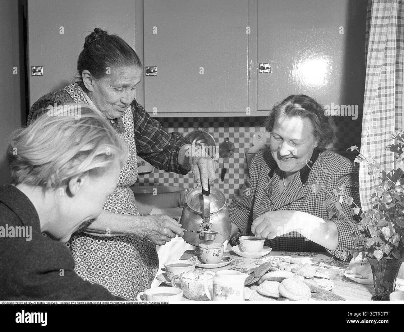 Casa della signora Anna Rösth (1879-1974) a Bollnäs, dove ospita ospiti per un caffè il 15 maggio 1953. Le belle coppe sono state preparate per i suoi visitatori. Con attenzione, versa il primo spruzzo attraverso un filtro nella sua tazza incrinata per assicurarsi che i fondi di caffè non raggiungano i suoi ospiti. Un piattino con biscotti assortiti, una caraffa panna e una ciotola da zucchero adornano il tavolo. Foto Stock
