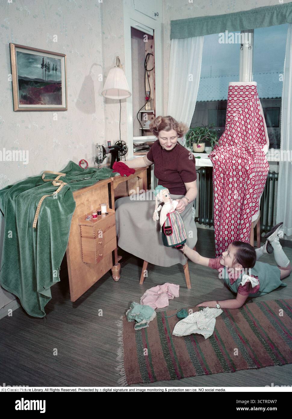 In una casa degli anni '1950, una madre e una figlia condividono un momento insieme. La classica macchina da cucire Husqvarna è orgogliosa di essere posizionata sul proprio tavolo, chiaramente ben utilizzata. Un armadietto per cucire nelle vicinanze contiene pratici cassetti per fili e tessuti. La figlia gioca con una grande bambola, cambiandone i vestiti. (1950s Conard Rev. BV98-2) Foto Stock
