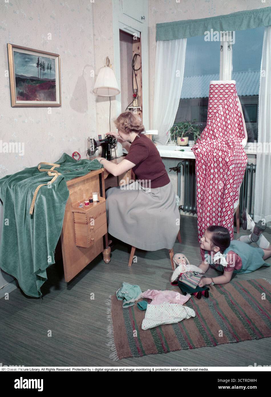 In una casa degli anni '1950, una madre e una figlia condividono un momento insieme. La classica macchina da cucire Husqvarna è orgogliosa di essere posizionata sul proprio tavolo, chiaramente ben utilizzata. Un armadietto per cucire nelle vicinanze contiene pratici cassetti per fili e tessuti. La figlia gioca con una grande bambola, cambiandone i vestiti. (1950s Conard Rev. BV98-3) Foto Stock
