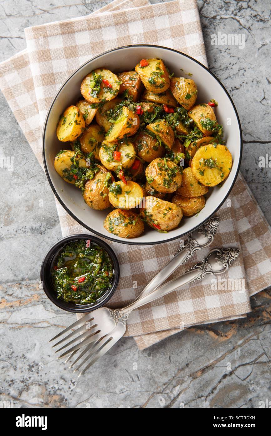 Patate novelle al forno servite con salsa chimichurri appena preparata da vicino in una ciotola sul tavolo. Vista dall'alto verticale Foto Stock