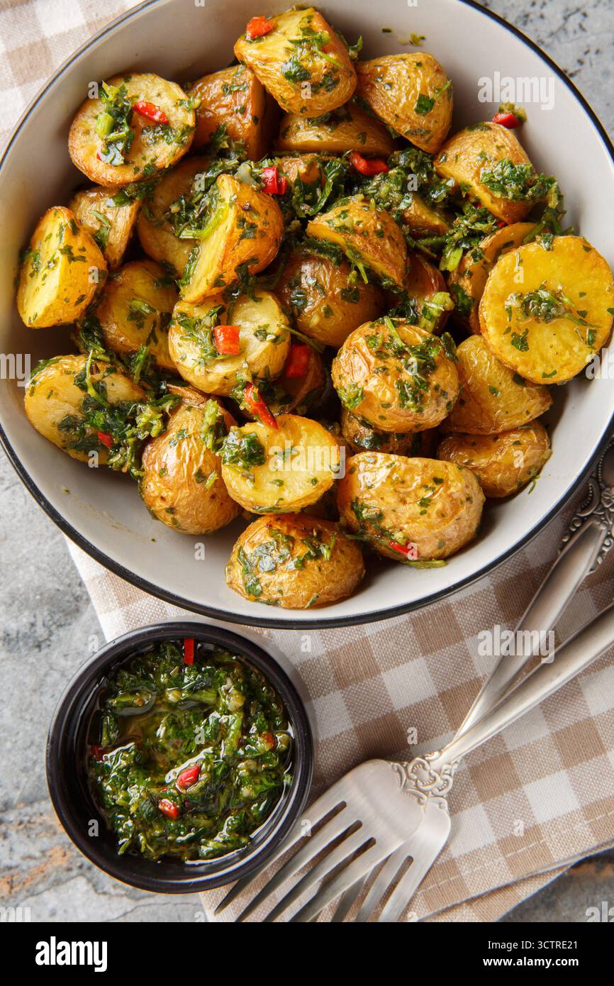Le patate arrostite dorate vengono gettate con una salsa chimichurri brillante e piccante sul piatto del tavolo. Vista dall'alto verticale Foto Stock