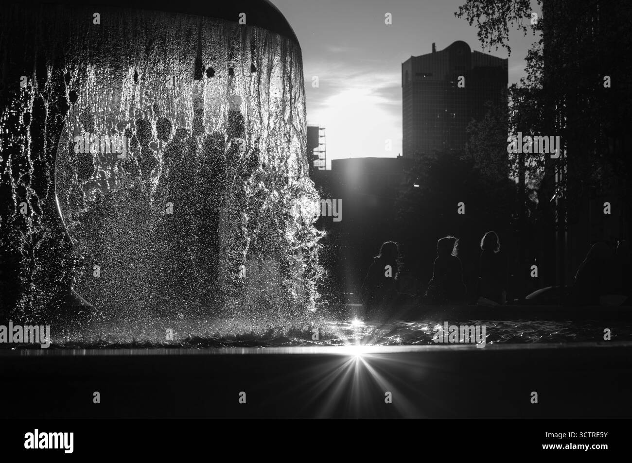 Urban Fountain sagoma al tramonto in un paesaggio urbano moderno - Fotografia editoriale in bianco e nero con luce e movimento Foto Stock