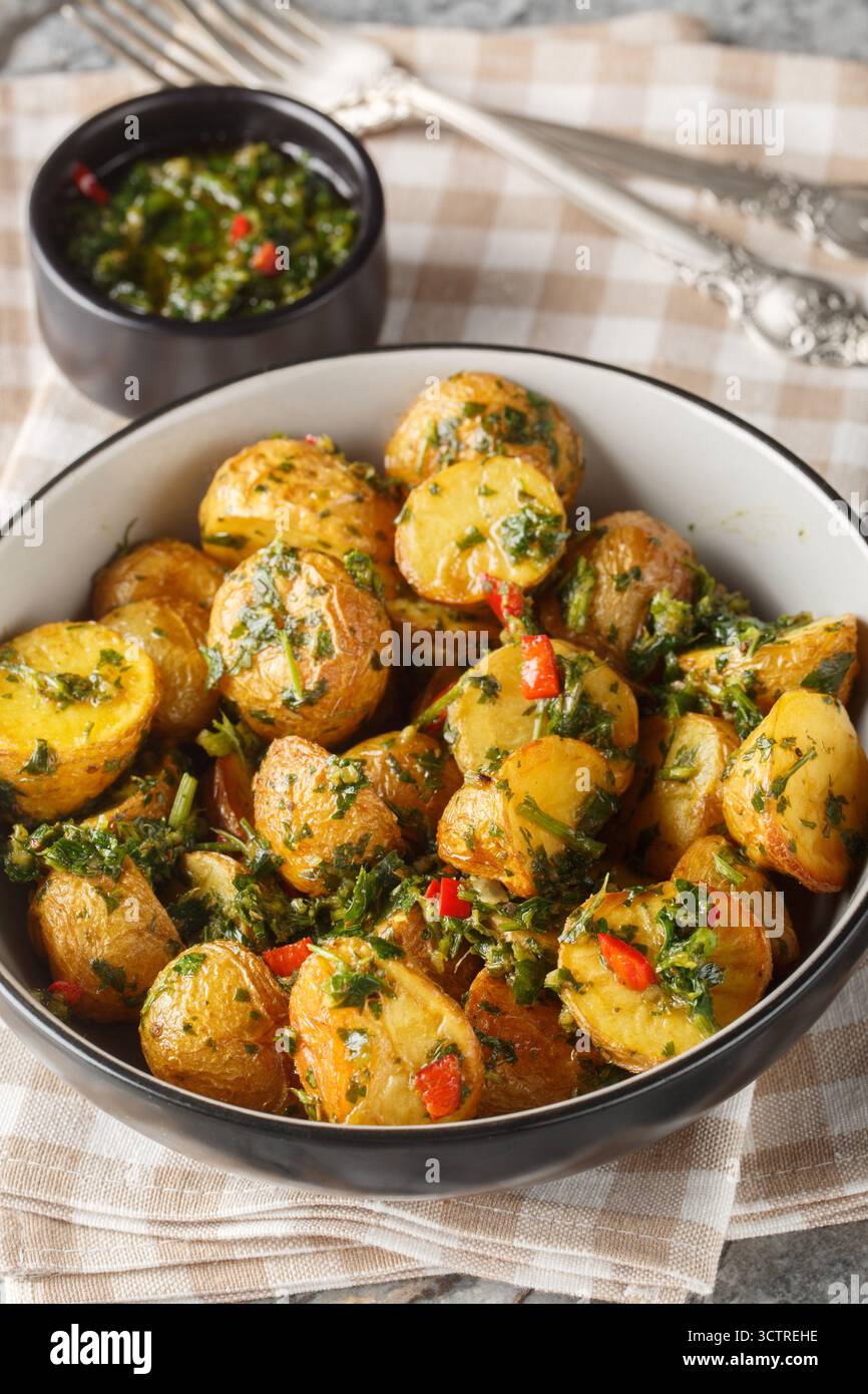 patate fritte croccanti tostate soffocate in una salsa piccante chimichurri preparata con prezzemolo fresco, aglio e origano in primo piano sul piatto del tavolo. Ve Foto Stock