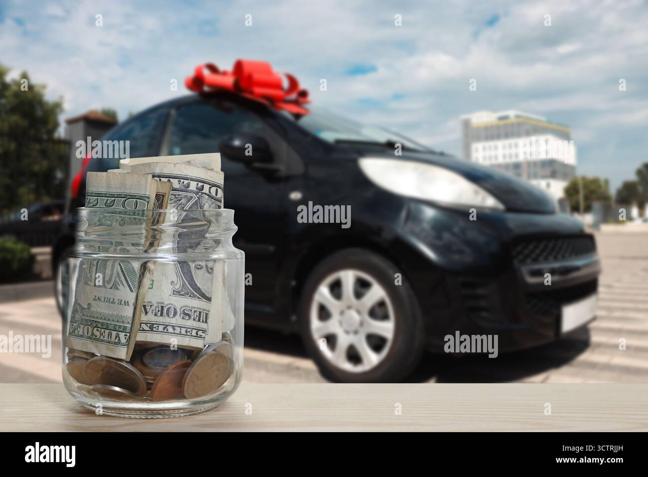 Dollari e monete in vaso contro auto con arco rosso all'aperto. Risparmia denaro per il veicolo Foto Stock