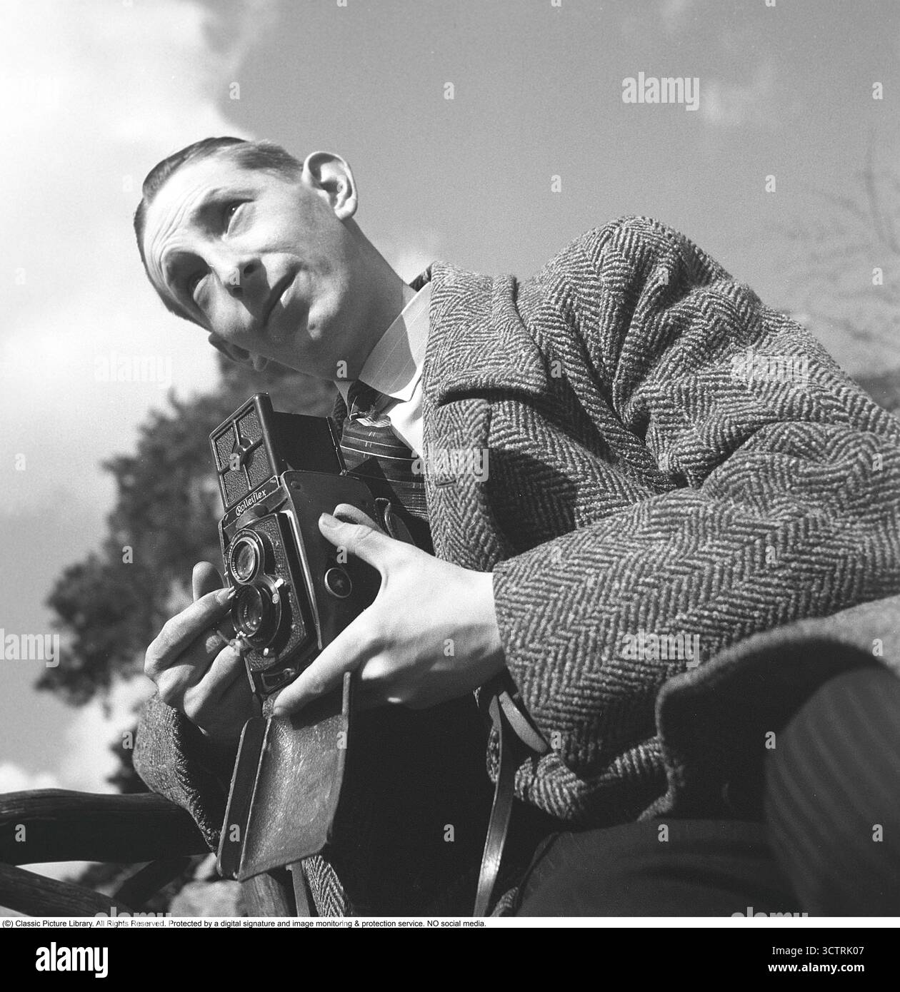 Fotografo di stampa Sven Malm a Skansen, aprile 1940, con la sua fotocamera Rolleiflex pronta. Questa fotocamera di medio formato, prodotta dalla ditta tedesca Franke & Heidecke (ora nota come Rollei), poteva catturare 12 esposizioni per rotolo su pellicola 6x6 cm. Il formato cinematografico, designato come "120" da Kodak, è diventato immensamente popolare tra i fotografi professionisti per la sua eccezionale qualità delle immagini e versatilità. Introdotta alla fine degli anni '1920, la Rolleiflex era rinomata per il suo design reflex a doppia lente, che forniva messa a fuoco e composizione precise. La sua struttura robusta e l'ottica nitida lo hanno reso un compagno affidabile Foto Stock