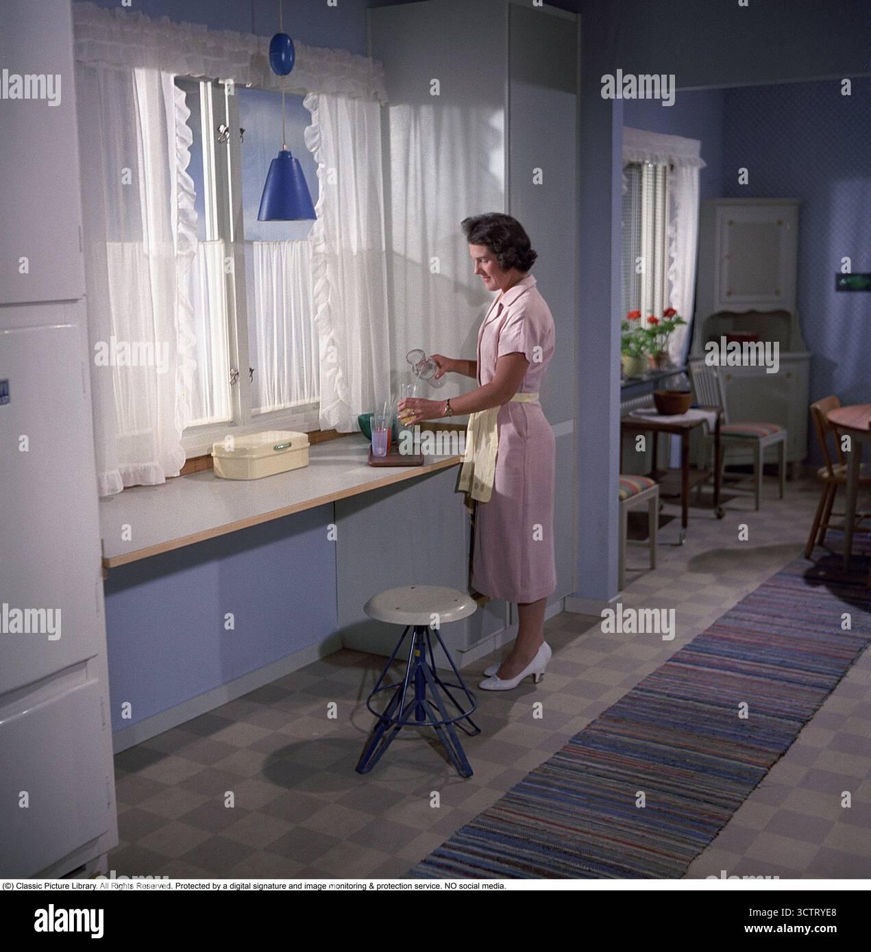 Nel 1958, una donna nella cucina di una casa Borohus, un simbolo del comfort domestico svedese. Borohus, un'azienda di costruzione di case che risale alla fine del XIX secolo, crebbe con il movimento della casa degli anni '1920. Fondata a Landsbro, Småland, il suo nome, abbreviazione di "Bo i ro i eget bo" (vivere pacificamente nella tua casa), rifletteva la sua etica. Come principale produttore svedese di case prefabbricate, Borohus prosperò con moduli, pareti e interni costruiti in fabbrica, tra cui cucine e armadi. Acquisita dalla cooperativa HSB nel 1936, ha operato fino al 1984. Nonostante i successivi fallimenti, i Borohu Foto Stock