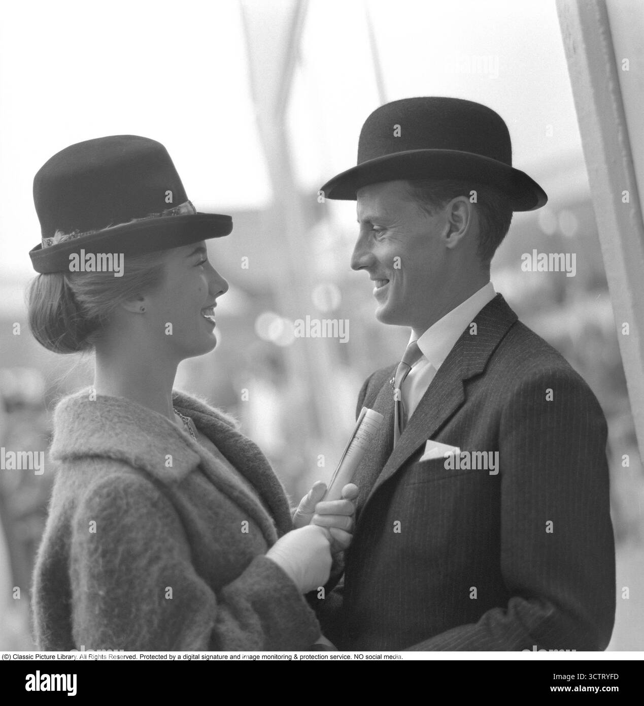 L'inaugurazione di Täby Galopp il 28 agosto 1960. Una coppia, elegantemente vestita per l'occasione, si guarda con abiti e cappelli raffinati. Durante le corse di cavalli degli anni '1960, era consuetudine vestirsi più formalmente del solito, con abiti, abiti e cappelli sartoriali che riflettono raffinatezza e tradizione. Foto Stock