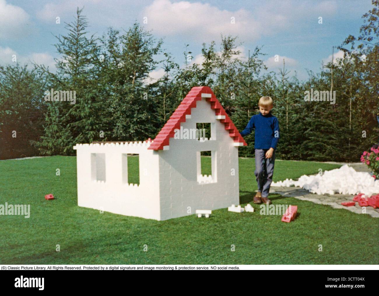 Lego gigante 1971. Il ragazzo nel giardino ha costruito una casa con pezzi giganti di lego. Le pareti e il tetto sono in costruzione. I pezzi sono di plastica, ma il produttore non è noto. Foto Stock