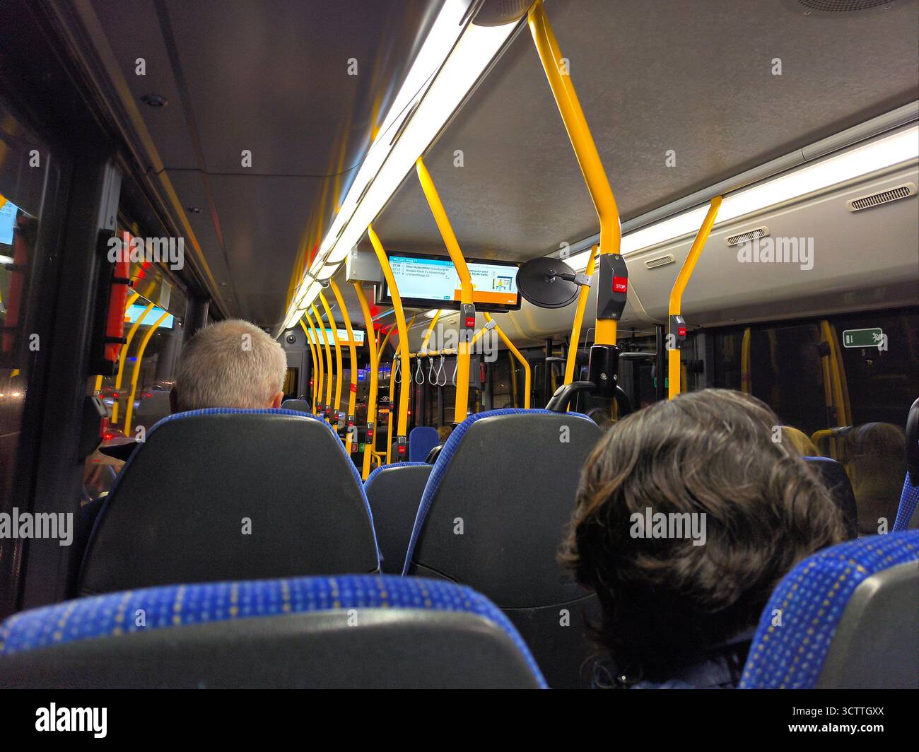 All'interno di un moderno City Bus: Posti a sedere blu, bastoncini gialli e passeggeri per un giro giornaliero Foto Stock