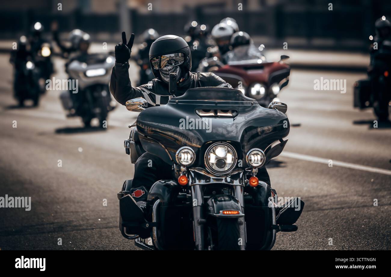 Un motociclista vestito di nero e una maschera cranica attraversano la città in una colonna motociclistica, creando un'immagine audace e suggestiva Foto Stock