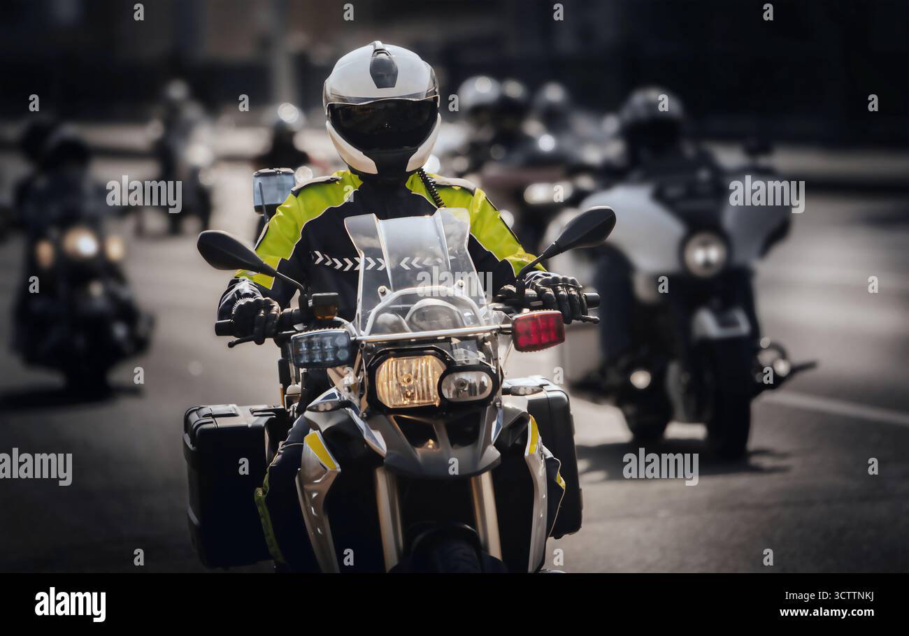 Un agente di polizia in uniforme e casco protettivo guida una motocicletta lungo la strada durante una sfilata o un servizio di pattuglia Foto Stock Un agente di polizia in uniforme e casco protettivo guida una motocicletta lungo la strada durante una sfilata o un servizio di pattuglia Foto Stock
