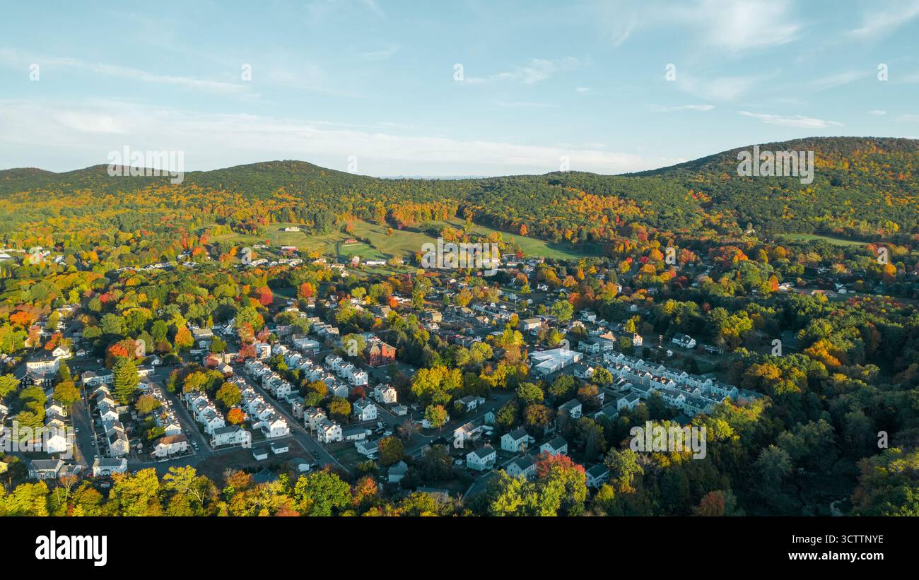 Vista aerea di una città annidata tra colline adornate da fogliame autunnale, che mostra un arazzo di colori caldi sotto un cielo luminoso, Easthampton, Massachusetts, Stati Uniti. Foto Stock