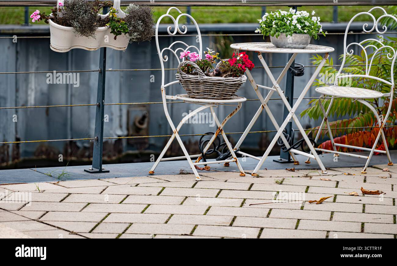 Giardino vicino alla casa, con fiori in pentole e mobili bianchi, design da strada all'aperto Foto Stock