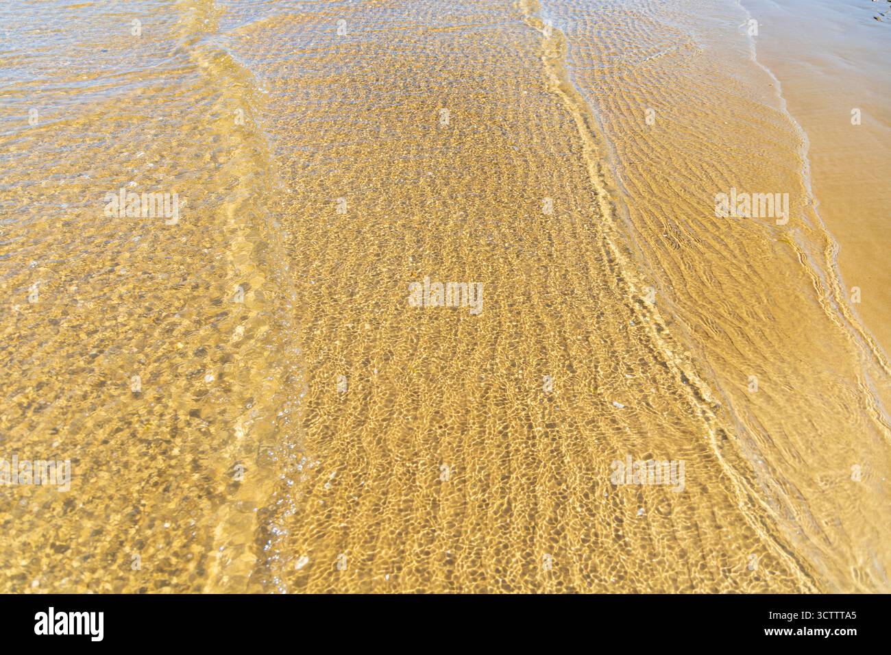 Intricate increspature di sabbia visibili sotto acque limpide e poco profonde con onde dolci, sulla tranquilla costa del Mar Baltico, creando un effetto astratto naturale Foto Stock