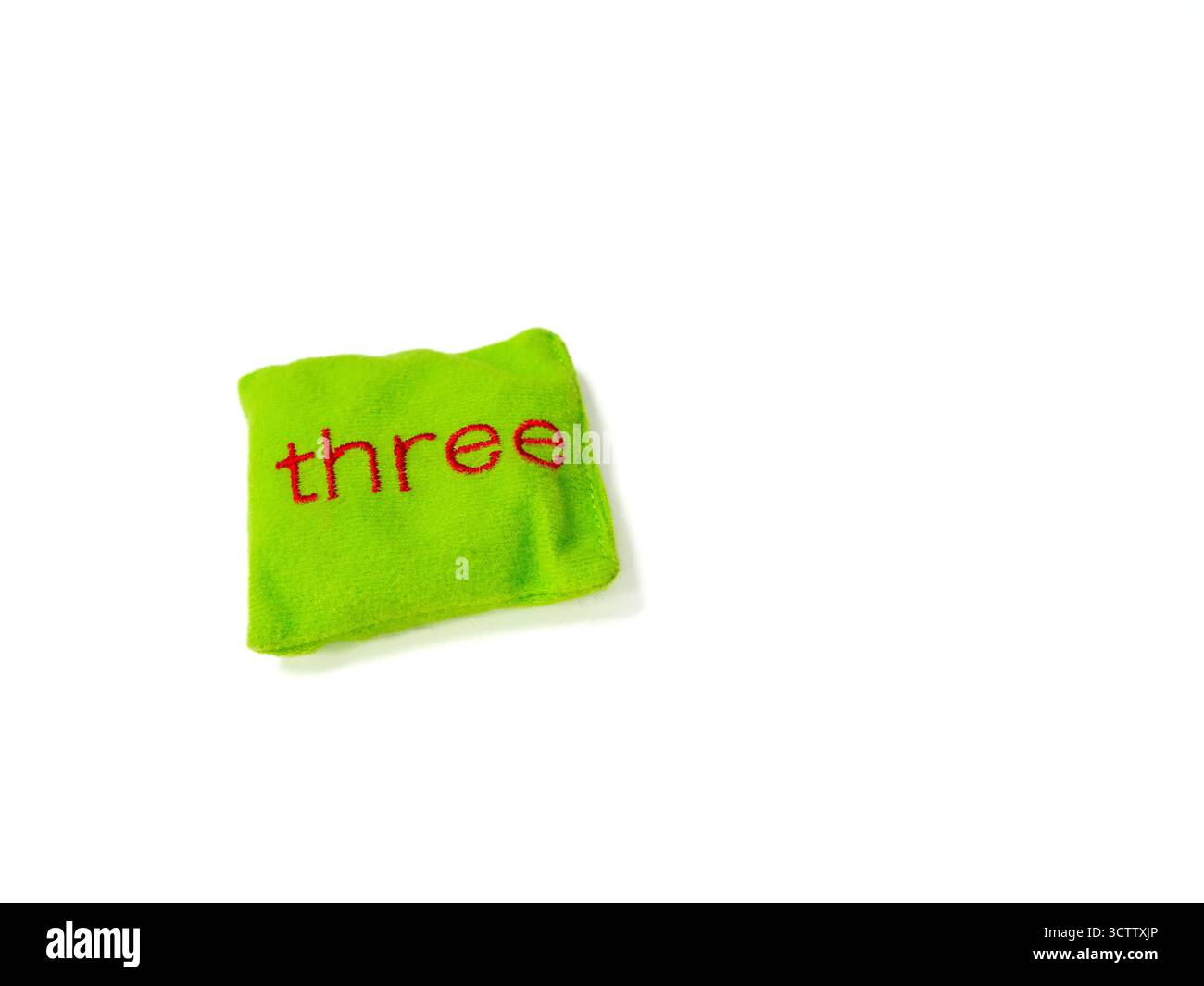Un sacchetto di fagioli verde brillante con la parola "tre" cucita in lettere rosse su sfondo bianco. Questo giocattolo in tessuto morbido è comunemente usato in earl Foto Stock