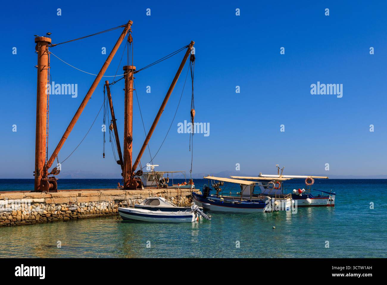 vista panoramica sul mare di barche da pesca ormeggiate sotto enormi paranchi di legno presso la pittoresca banchina di pietra nel villaggio di pescatori greco di moutsouna Foto Stock
