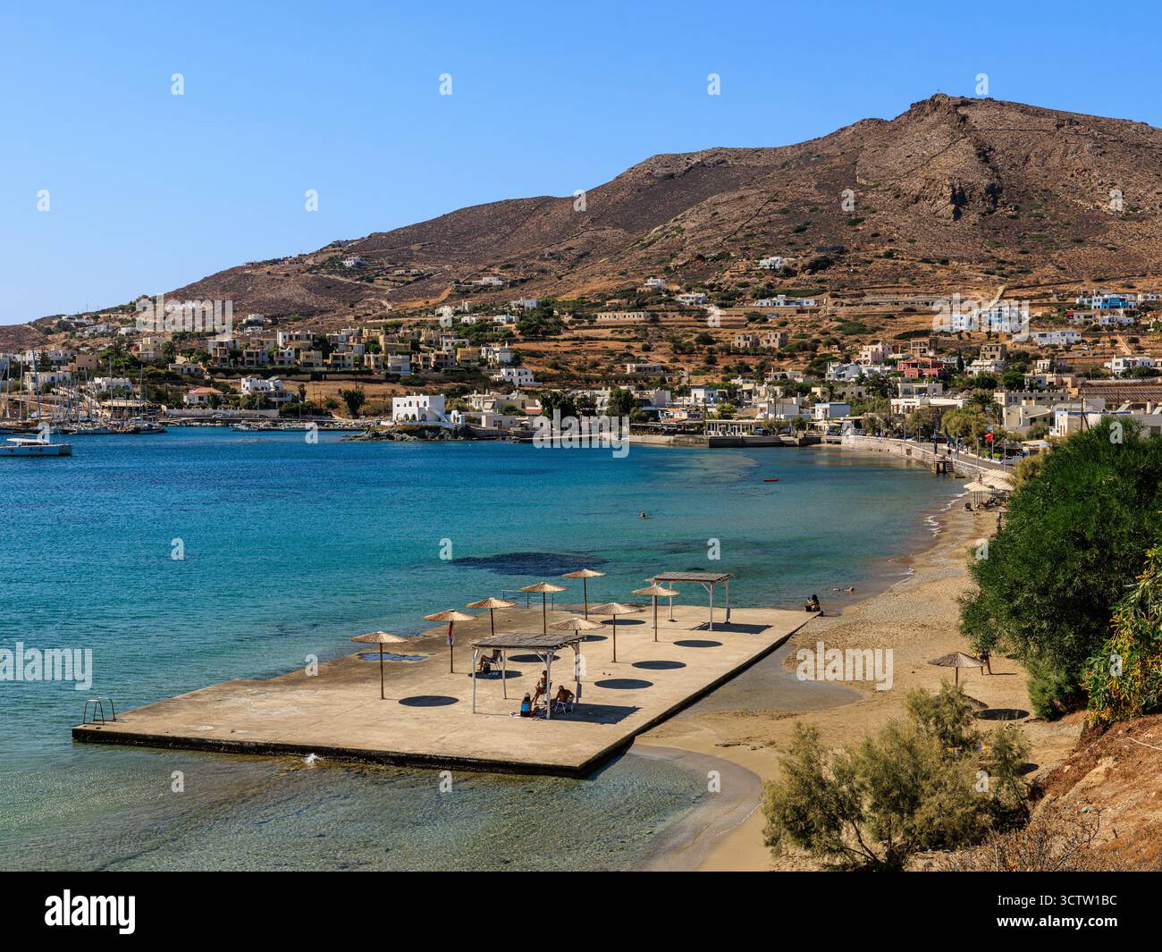 tranquillo villaggio costiero con spiaggia in piattaforma che aspetta gli amanti del sole al mare calmo in una giornata soleggiata sull'isola greca Foto Stock