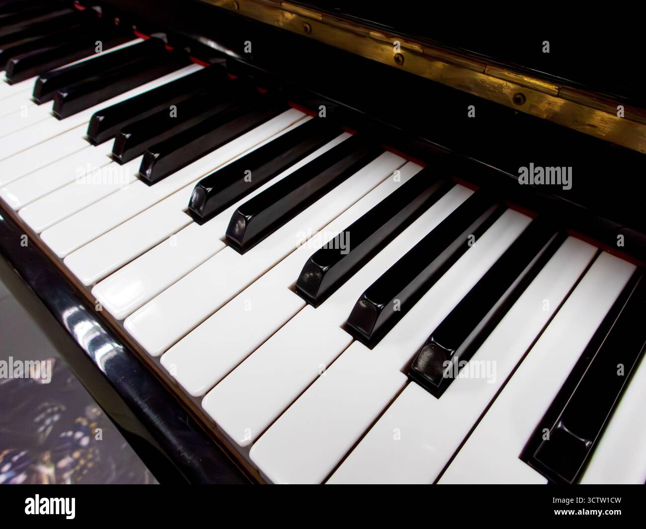 Vista laterale ravvicinata dei tasti piano in bianco e nero lucido con il riflesso del bordo in ottone dorato da un angolo basso con una profondità di campo ridotta. Foto Stock