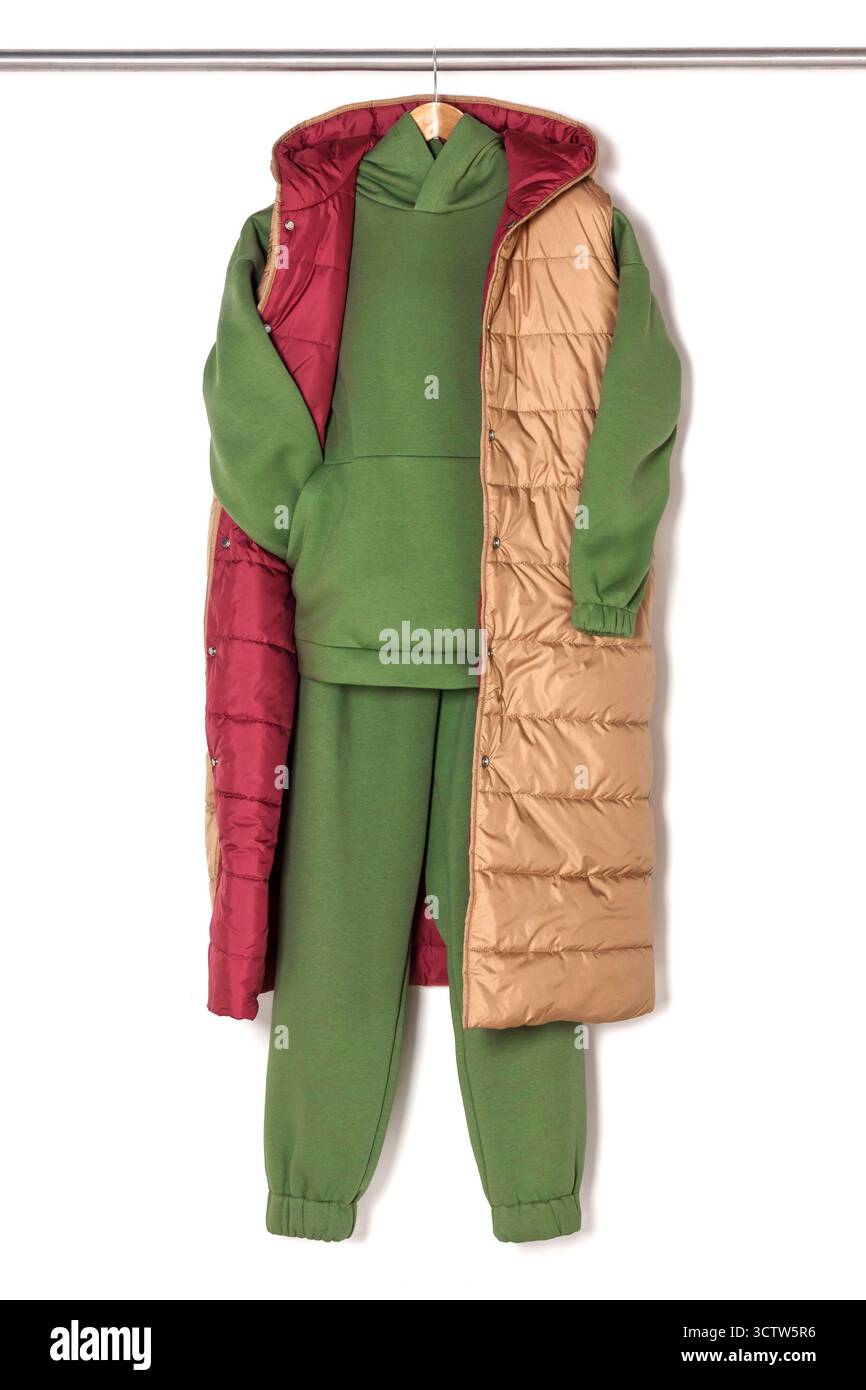 Felpa e pantaloni verdi, con cappuccio e oliva, abbinati a un lungo gilet beige con fodera rossa su sfondo bianco. Comfort e calore, elegante e Foto Stock