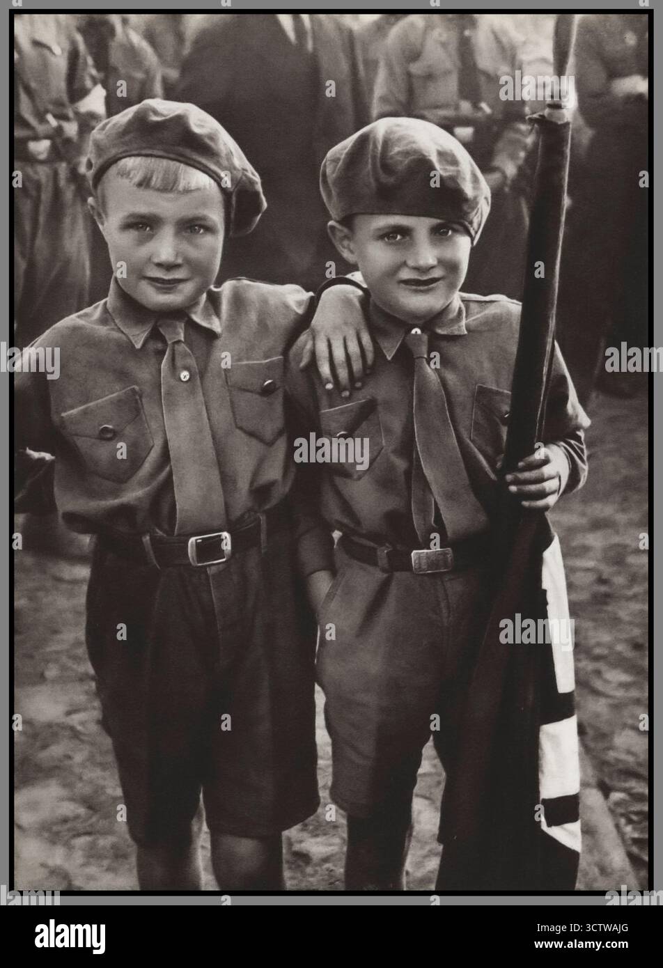 HITLERJUGEND due neonati membri in uniforme della Gioventù hitleriana con una bandiera di svastica. Da una pubblicazione di propaganda nazista del 1935, Jugend um Hitler. I bambini di età compresa tra i 10 e i 14 anni entrarono a far parte del ramo junior «Jungvolk», noto come «Pimpfe». Raduno nazista negli anni '1930 della Germania nazista Foto Stock