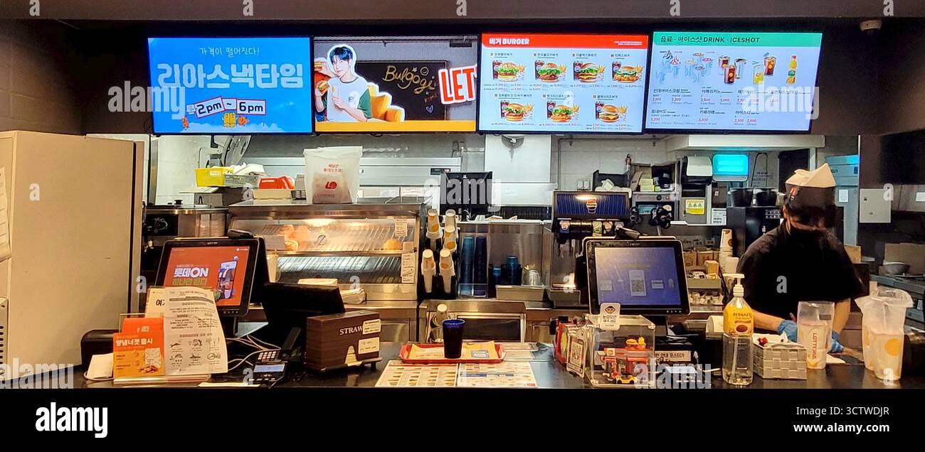 Una fotografia di un ristorante fast food nella periferia di Busan, Corea del Sud, che presenta un banco di servizio con menu digitali, che include una pubblicità con un idolo K-pop per un "Bulgogi Burger" (?? ??, Bulgogi Beogeo). Lotteria, un'importante catena di fast-food dell'Asia orientale, usa spesso idoli K-pop popolari per le sue campagne pubblicitarie per attirare un pubblico più giovane. 2025. Foto Stock