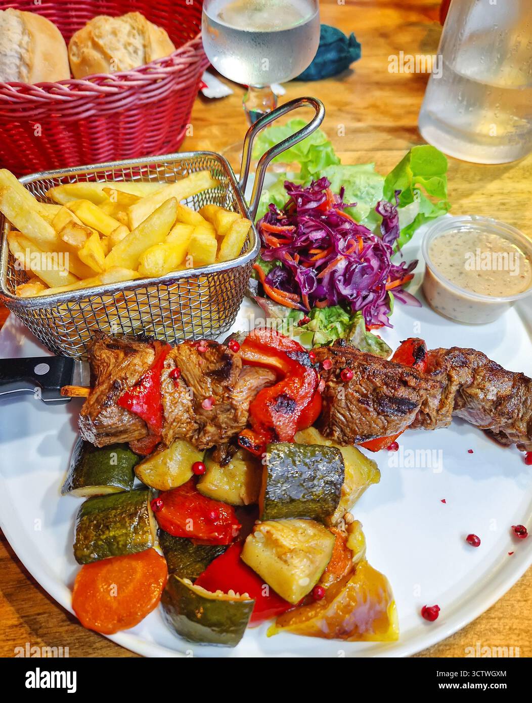 Primo piano di un piatto con brochette barbecue di carne alla griglia e pepe su uno spiedino di coltelli servito con verdure mediterranee arrostite e un cesto Foto Stock