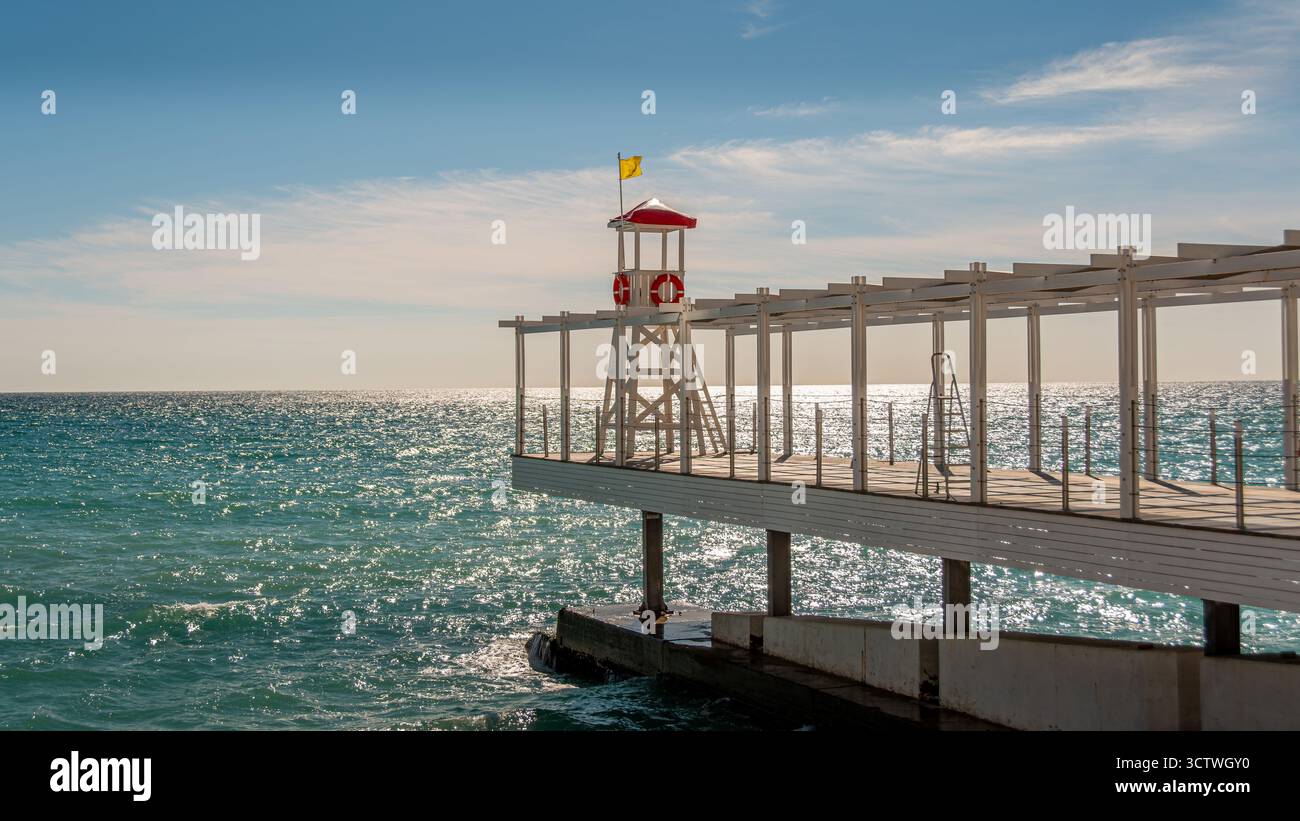 Sedia bagnino alla fine di un molo sopra la spiaggia in una località balneare al tramonto. Concetti di viaggio di piacere e vacanza al mare. Niente persone Foto Stock