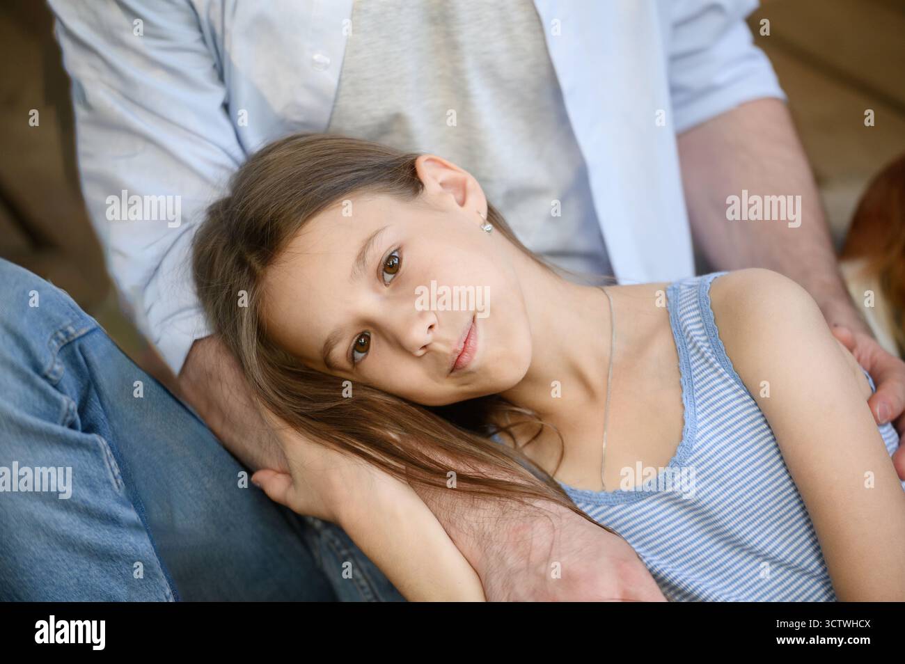 Primo piano di una figlia sdraiata in grembo del padre mentre siede sul portico di una casa di campagna in legno. Papà abbraccia, accarezza ragazza, esprimendo amore e cura. Genitorialità single, supporto e fiducia tra genitore e figlio Foto Stock