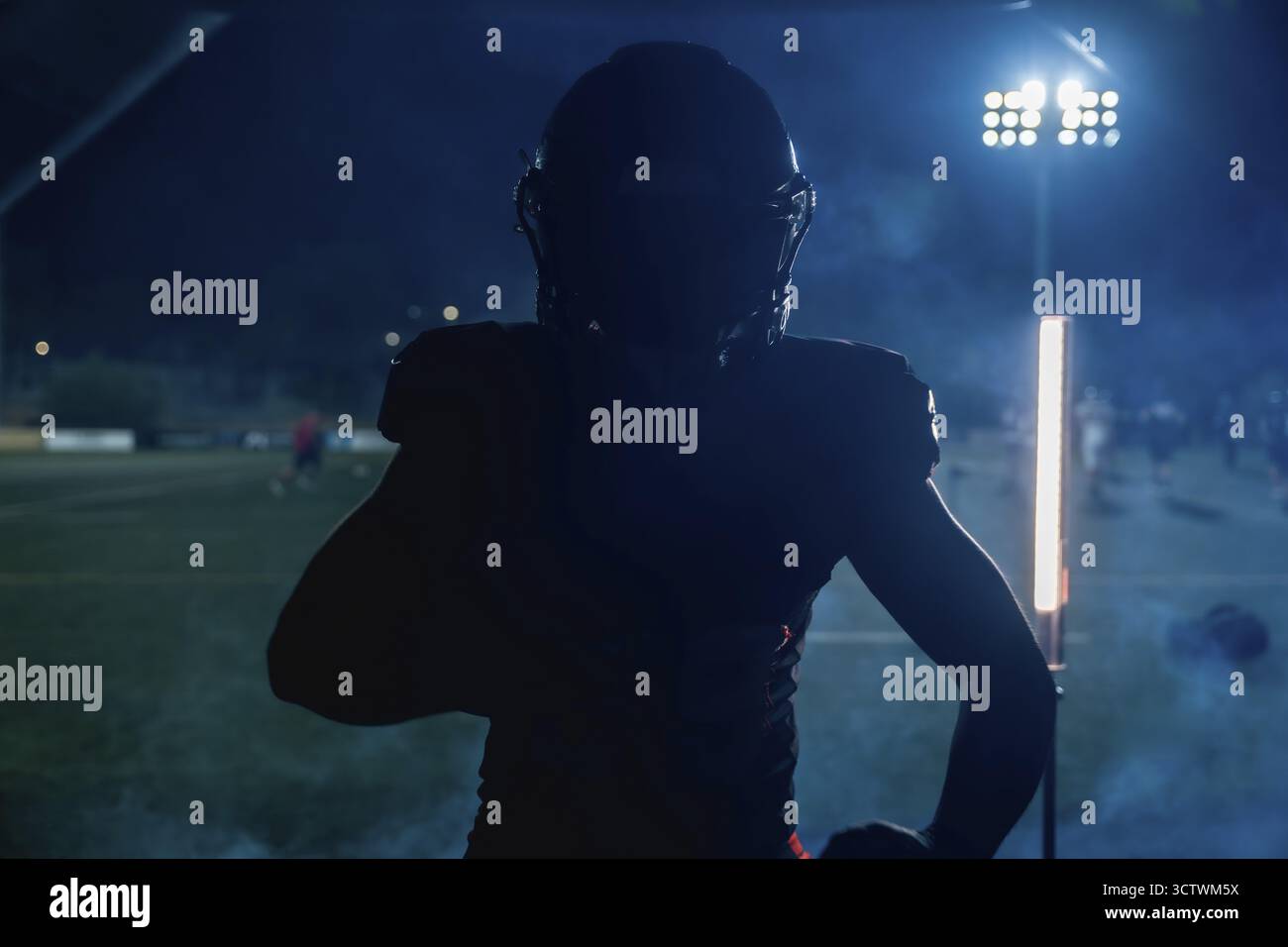 Giocatore di football americano in piedi in silhouette su un campo buio sotto le luci luminose dello stadio di notte, creando un'atmosfera suggestiva durante un intenso periodo Foto Stock