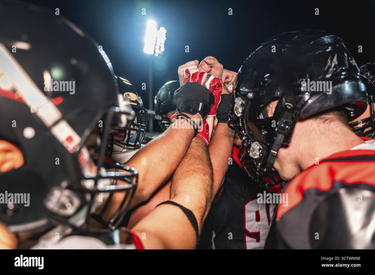 Giocatori di football americano che mettono le mani insieme in un huddle, simboleggiano il lavoro di squadra, l'unità, la strategia e la motivazione su un campo durante una partita notturna Foto Stock