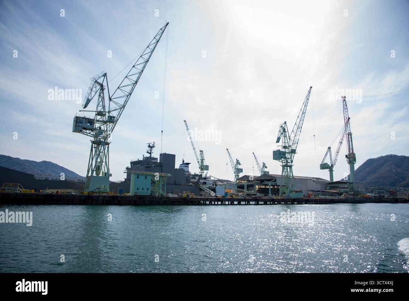 Cantiere navale industriale in Giappone con gru alte e navi attraccate lungo il lungomare in una giornata di sole. Foto Stock