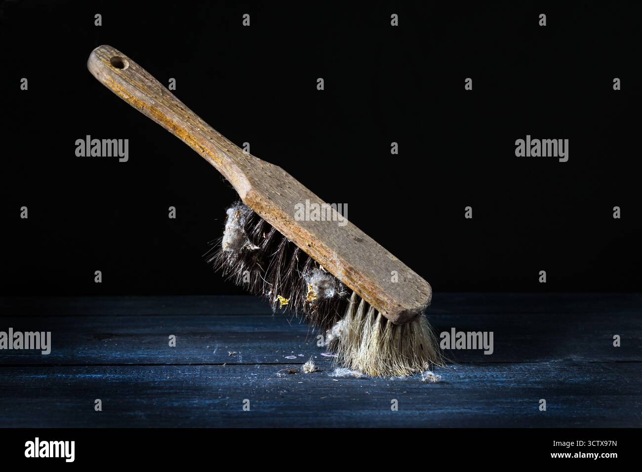 Vecchia spazzola manuale con manico in legno usurato e setole naturali con molti coniglietti di polvere, appoggiata su uno sfondo scuro, natura morta, pulizia vintage u Foto Stock