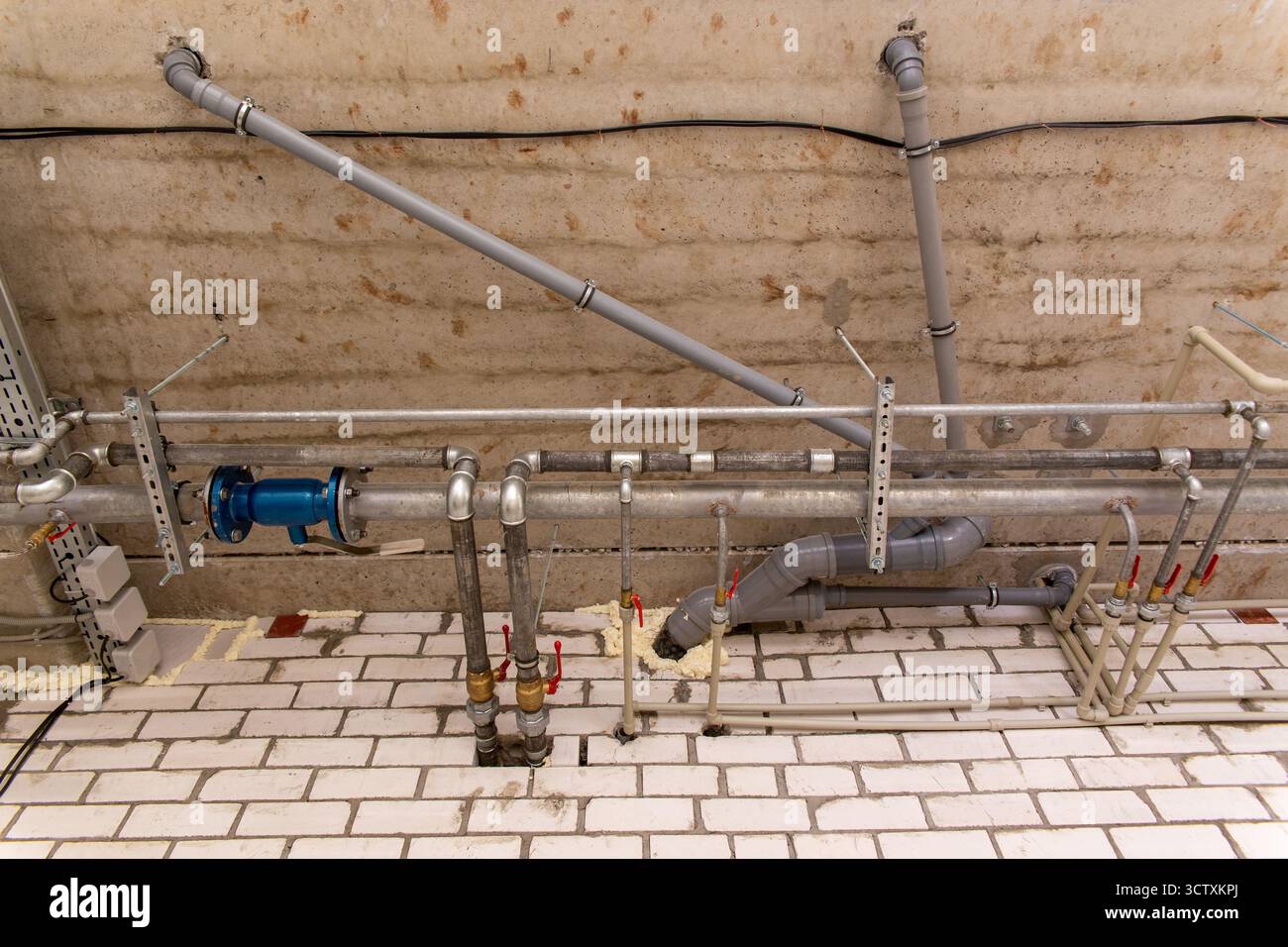 Impianto idraulico e di riscaldamento industriale sopraelevato con una rete di tubi dell'acqua in metallo, valvole e linee di drenaggio in plastica sotto il soffitto di una fabbrica. Foto Stock