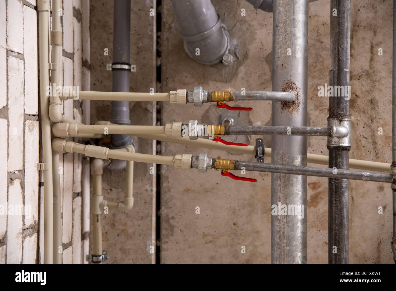Impianto idraulico e di riscaldamento industriale sopraelevato con una rete di tubi dell'acqua in metallo, valvole e linee di drenaggio in plastica sotto il soffitto di una fabbrica. Foto Stock