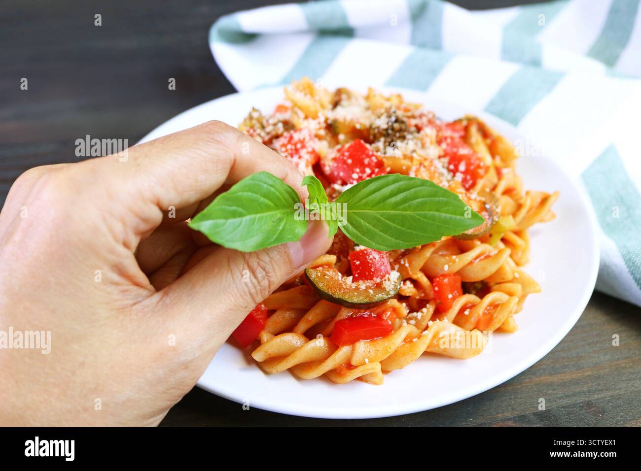 Mettere a mano le foglie di basilico su un piatto di Fusilli di grano intero appena cucinati in salsa di pomodoro Foto Stock