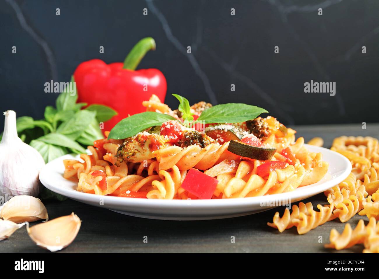 Deliziosa pasta Fusilli di grano intero in salsa di pomodoro con i suoi ingredienti sparsi intorno Foto Stock