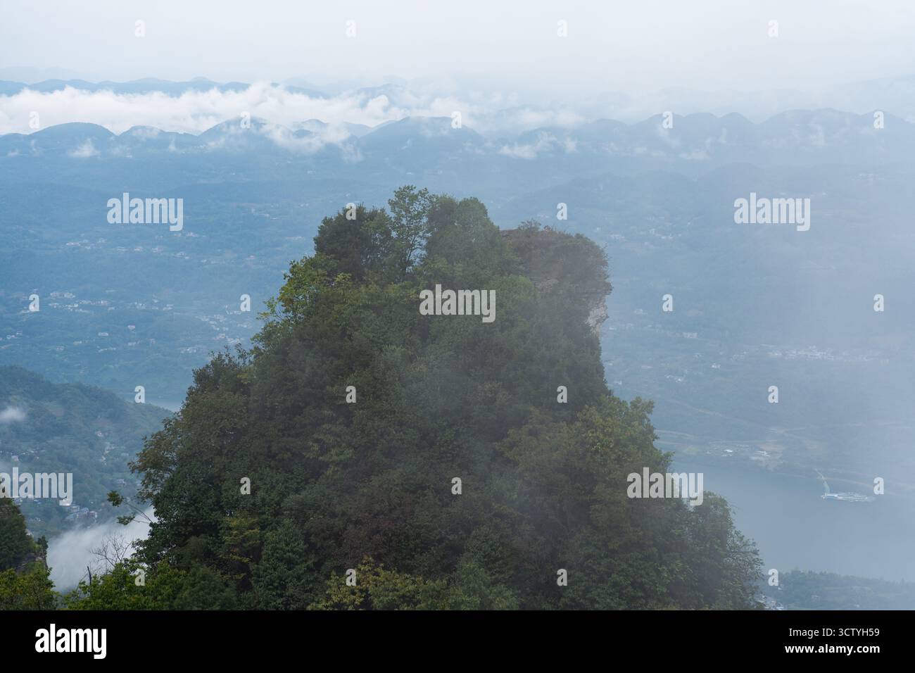 Le montagne nebbiose sorgono sopra gli alberi e una città sottostante in Cina. Foto Stock