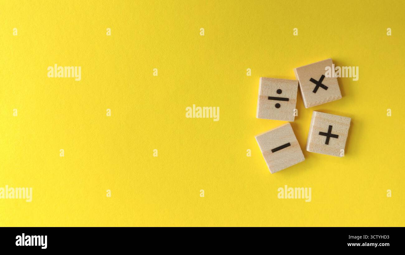 Simboli di funzionamento aritmetico fondamentali su blocchi di legno sparsi su uno sfondo giallo brillante con spazio di copia. Foto Stock