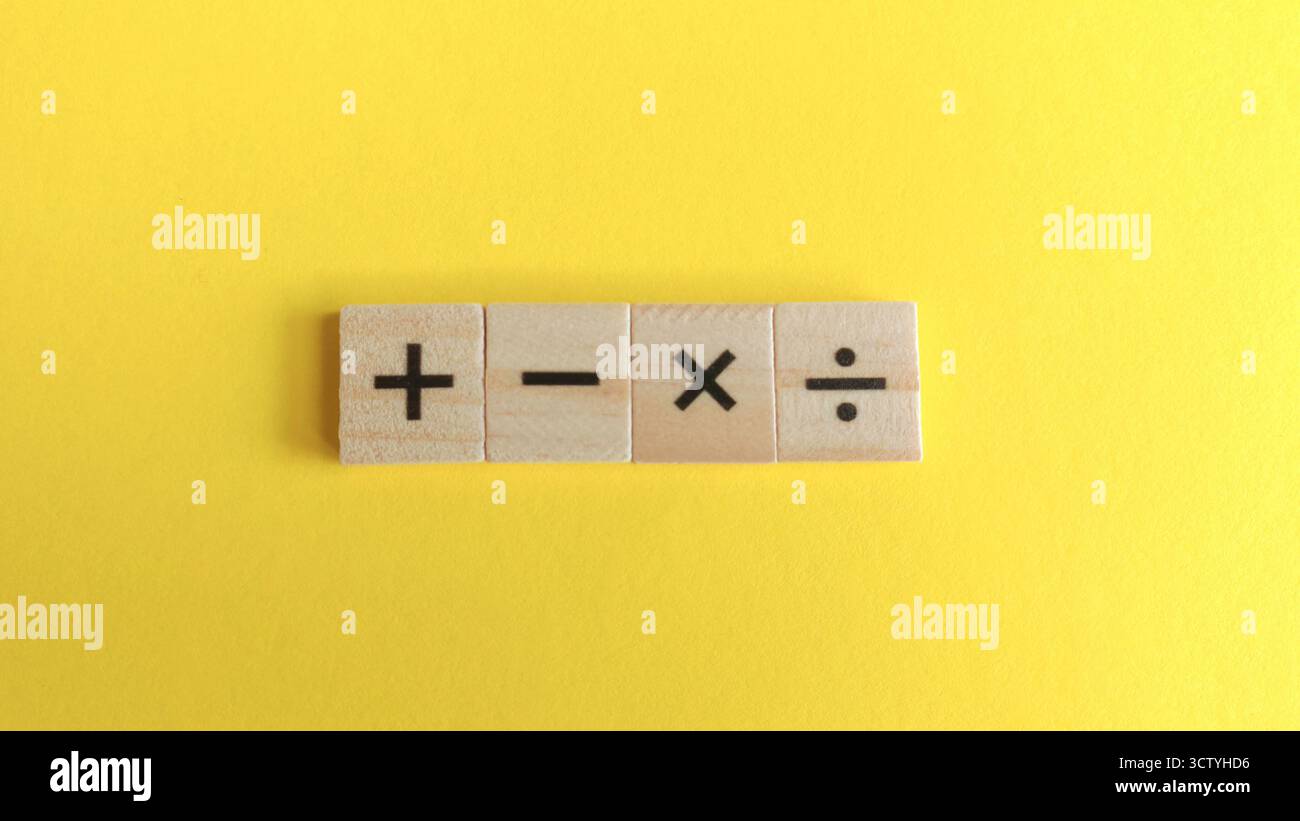 Quattro segnali di funzionamento matematico su blocchi di legno allineati su un sfondo giallo brillante per temi educativi e finanziari. Foto Stock