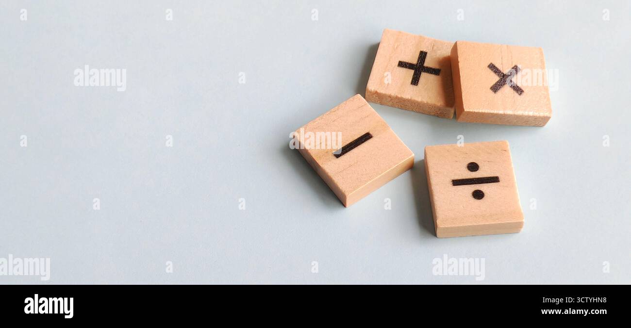 Simboli aritmetici fondamentali su blocchi di legno sparsi su un morbido sfondo blu con spazio di copia pulito per temi educativi e finanziari. Foto Stock