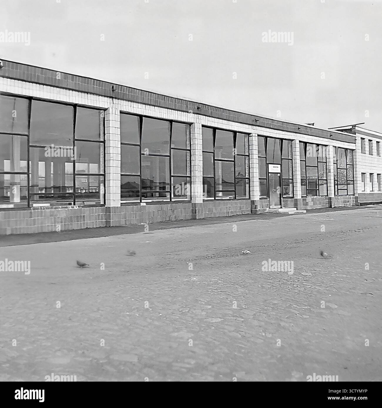 L'esterno di un nuovo mercato coperto a Sloviansk, la RSS Ucraina, viene catturato in questa foto architettonica in bianco e nero del 1970. Il lungo padiglione a un piano è un ottimo esempio di architettura modernista sovietica, caratterizzato da un tetto piatto, una facciata rivestita in piastrelle di colore chiaro e un motivo ritmico di grandi finestre panoramiche. L'estetica pulita, funzionale e geometrica dell'edificio è prominente. Questa immagine documenta un pezzo significativo di infrastruttura pubblica dell'era Brezhnev, mostrando lo stile e la portata dello sviluppo urbano Foto Stock