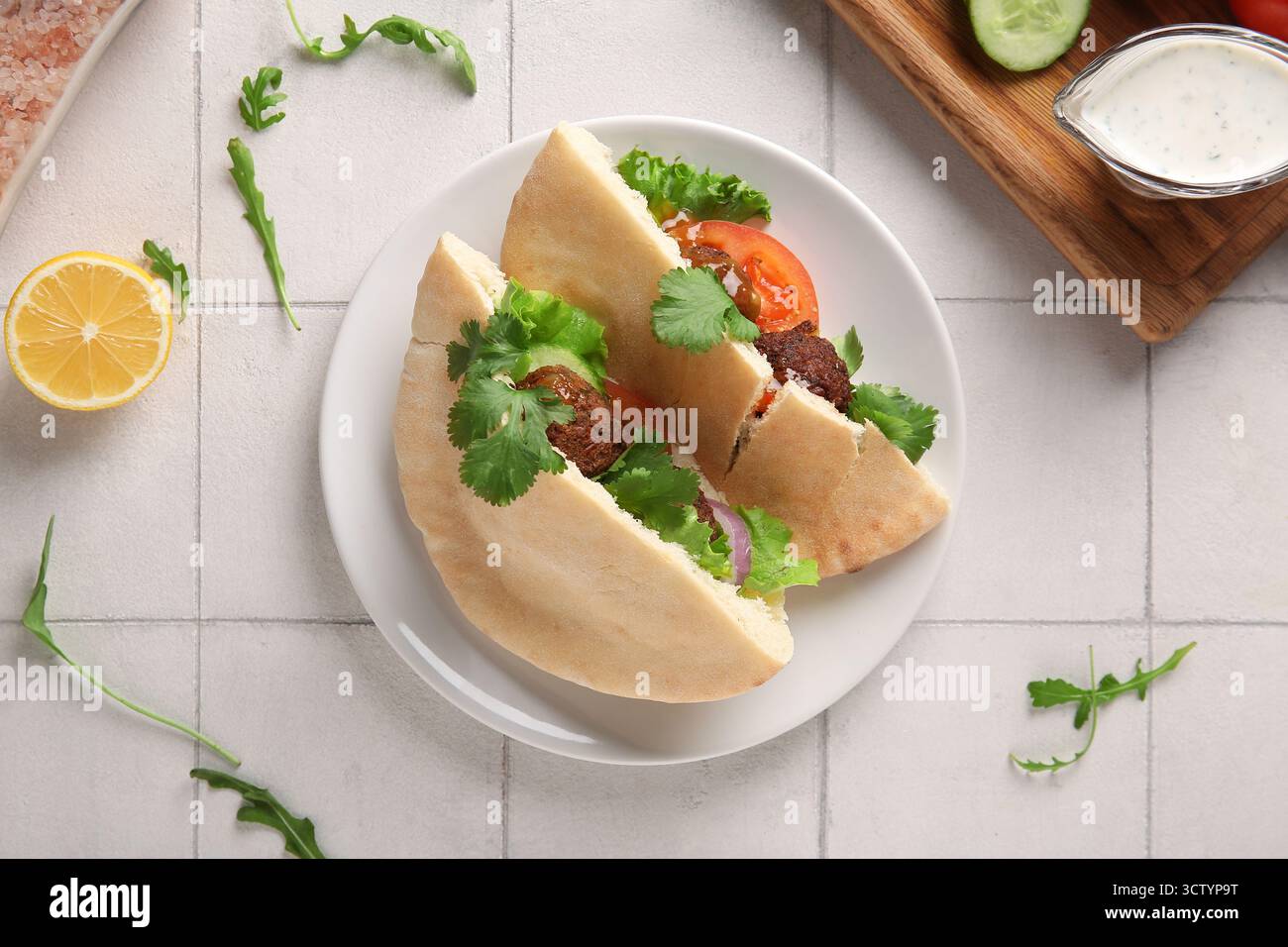 Piatto di deliziose pitas con falafel e verdure fresche su sfondo piastrellato bianco Foto Stock