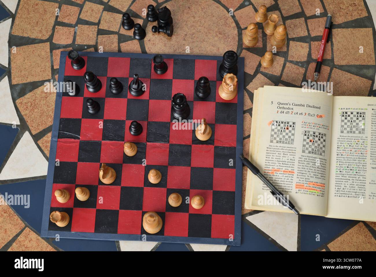 Imparando l'agilità mentale, gli scacchi del gambetto della regina si aprono usando un libro di scacchi e un set di scacchi vintage con scacchiere Staunton Foto Stock