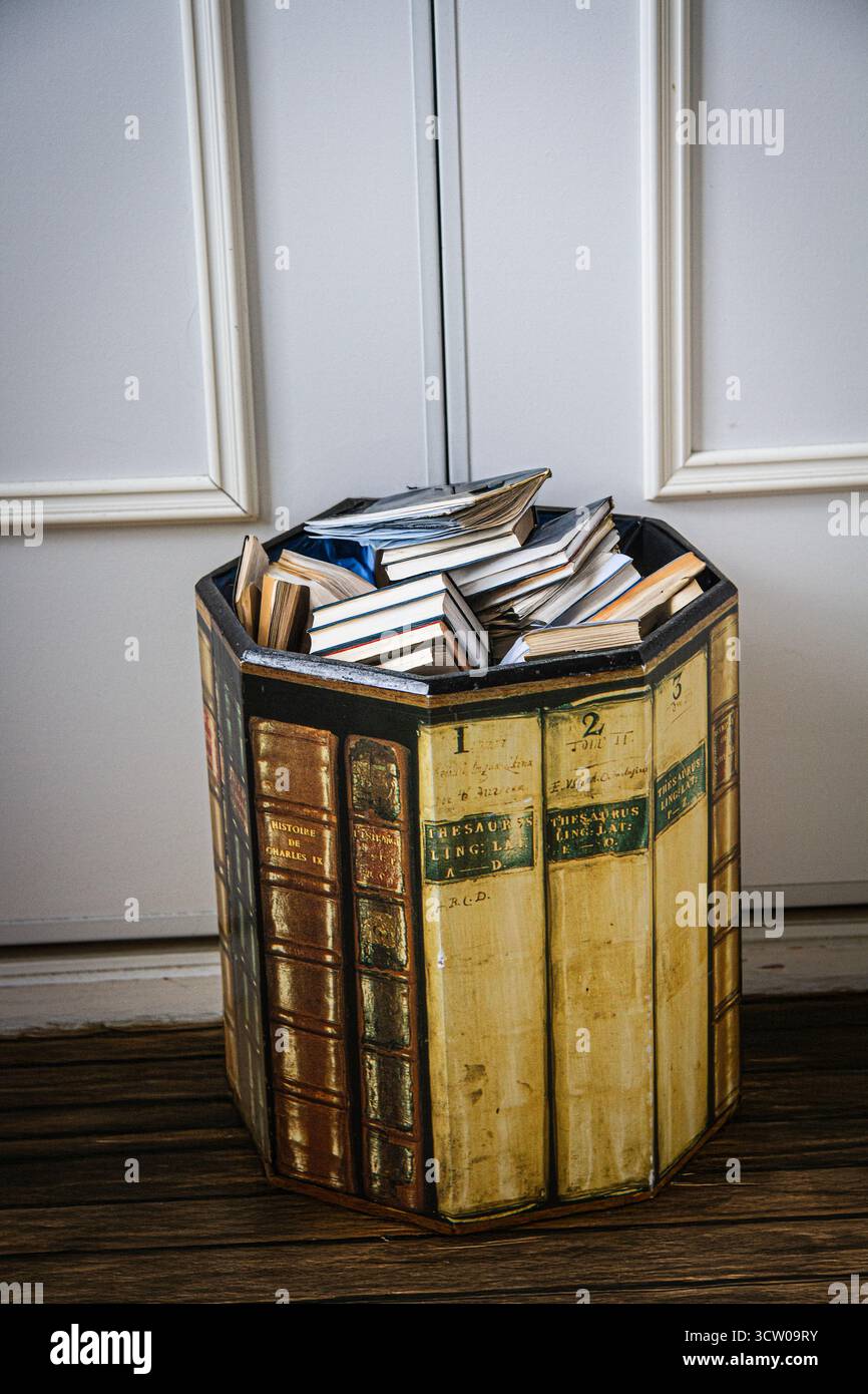 Un cestino per rifiuti domestici rivestito in pannelli multipli decorato per sembrare un gruppo di estremità di libri e pieno di libri scartati Foto Stock