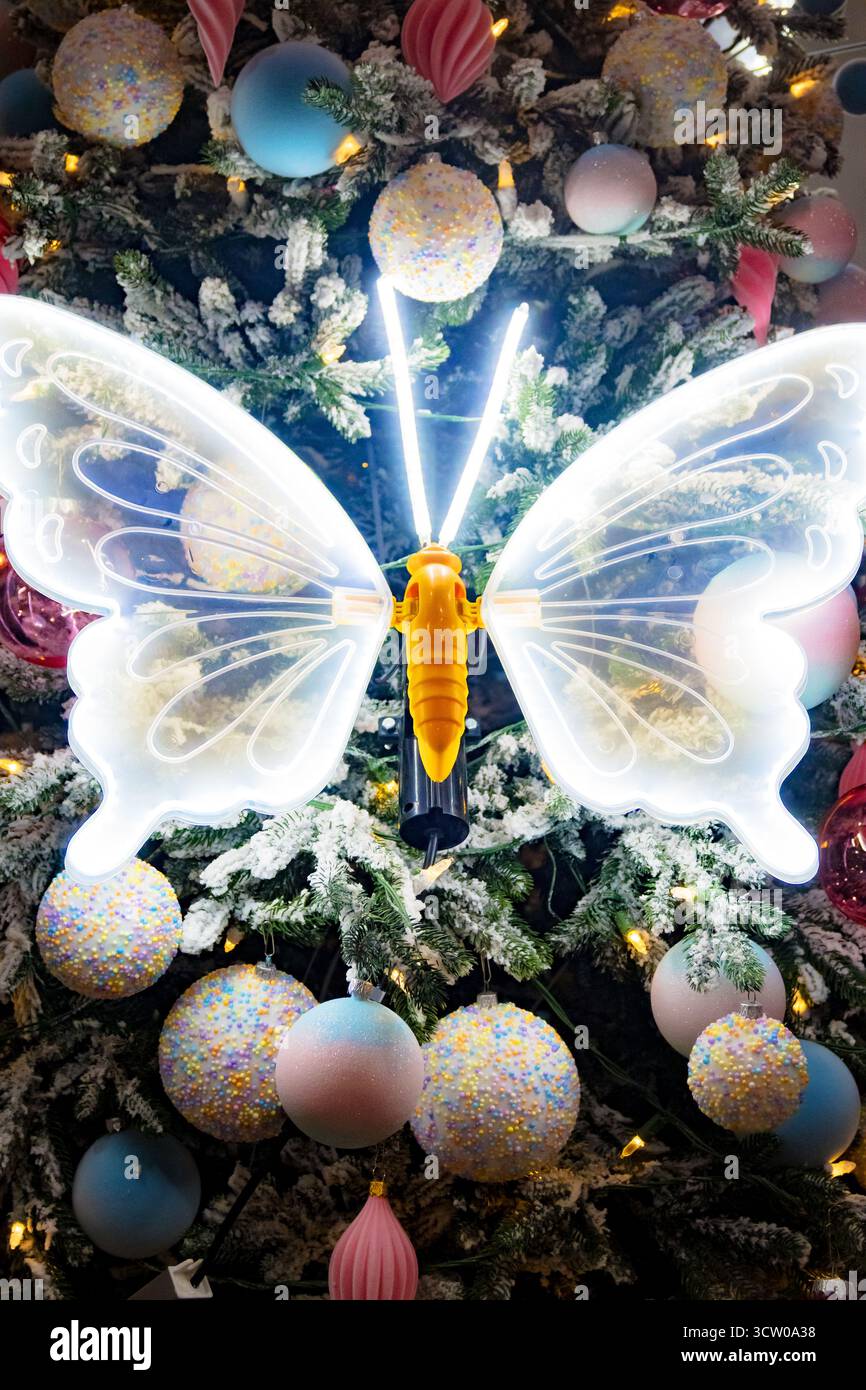 Un albero di Natale splendidamente decorato occupa il centro della scena, caratterizzato da un suggestivo ornamento a farfalla al neon che aggiunge un tocco moderno e stravagante Foto Stock